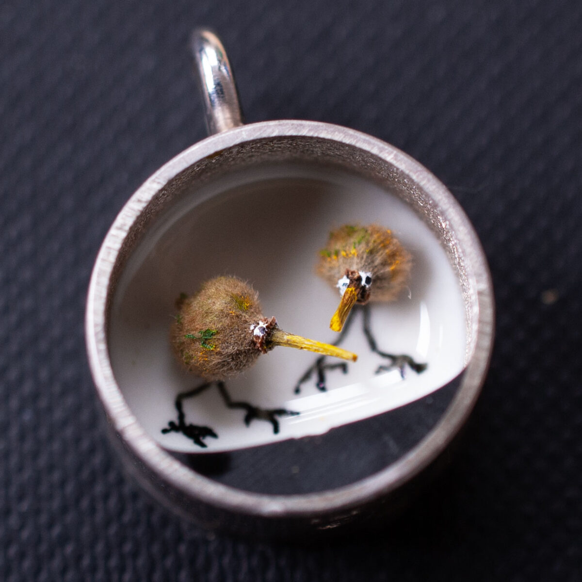 Nahaufnahme Kettenanhänger, 1,5 cm. Die Fläche ist gestaltet mit Samen von Linden, die zu Vögeln umgedeutet sind