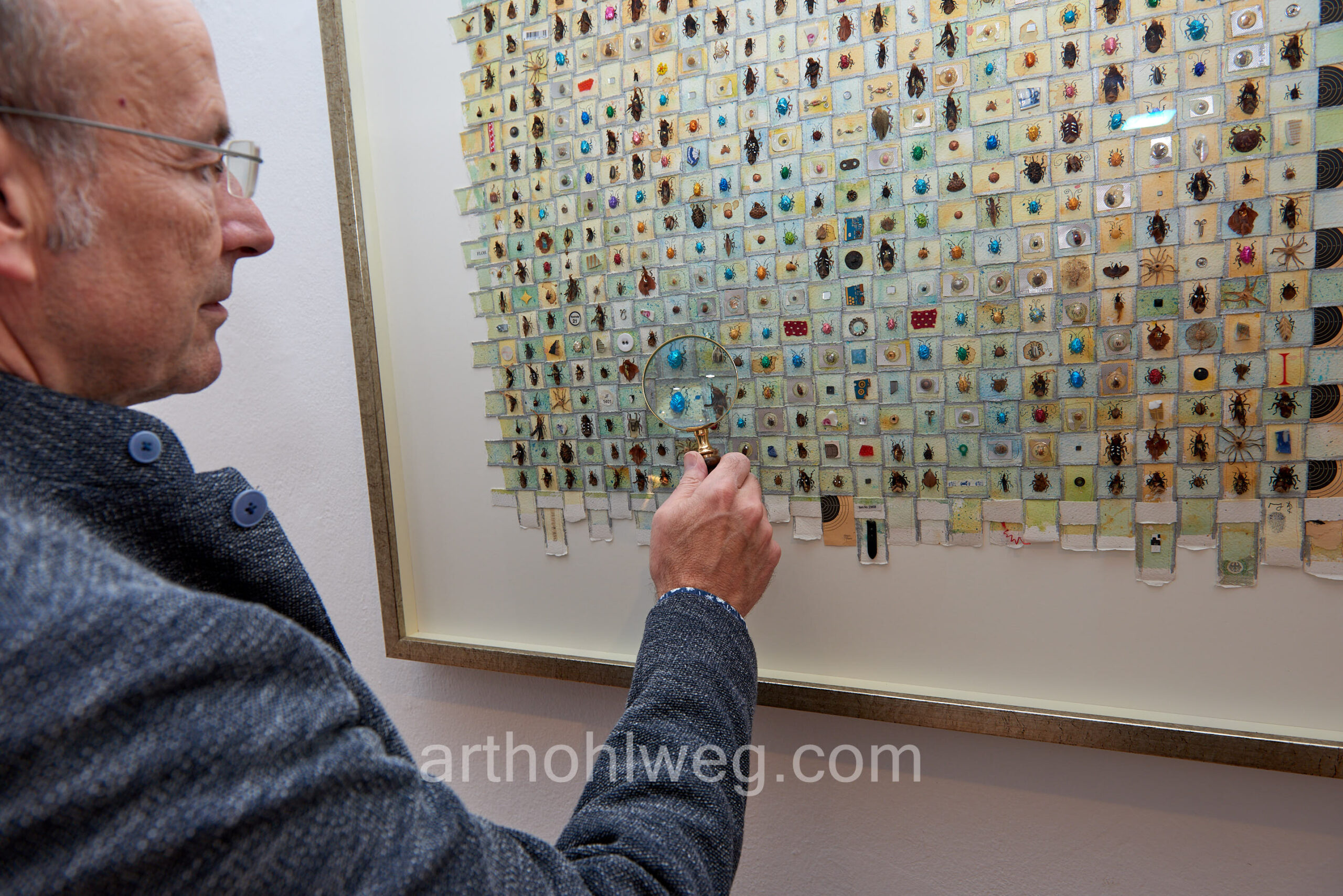 Person holds magnifying glass over large collage of small found objects