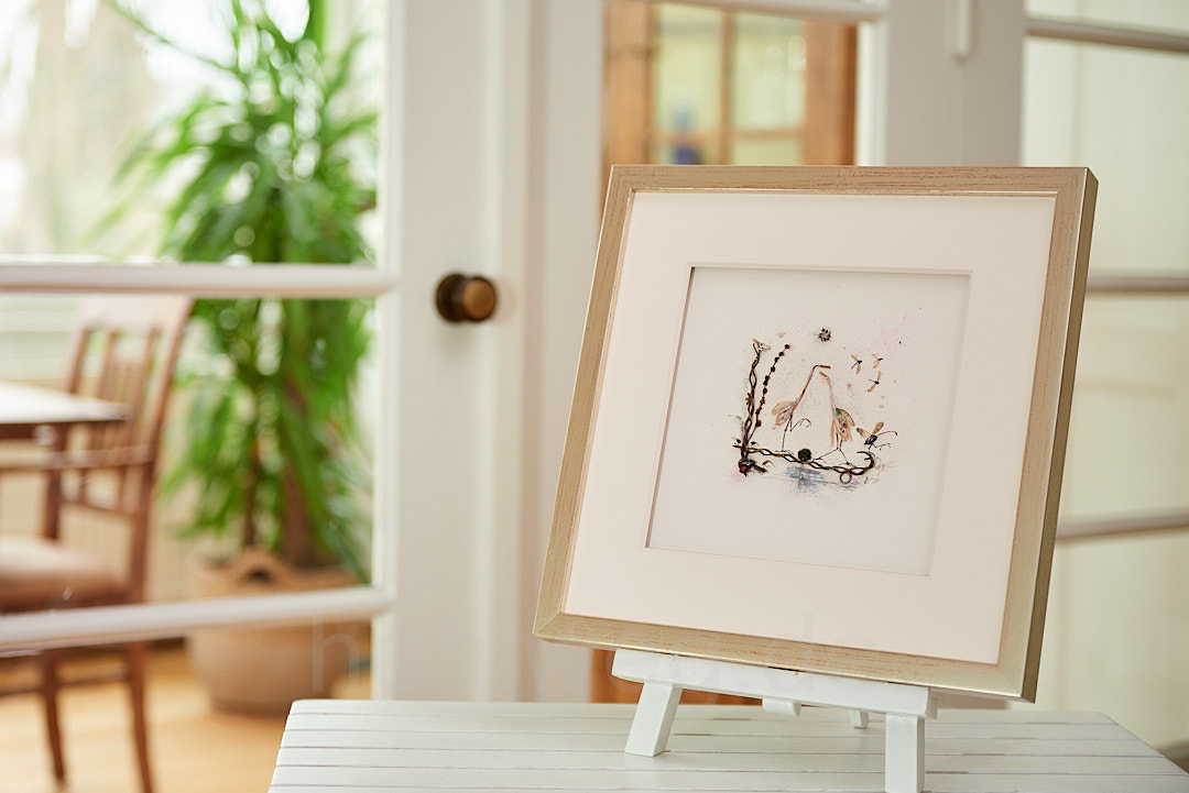 Framed collage by Magdalena Hohlweg presented on easel in room with stylish ambience.