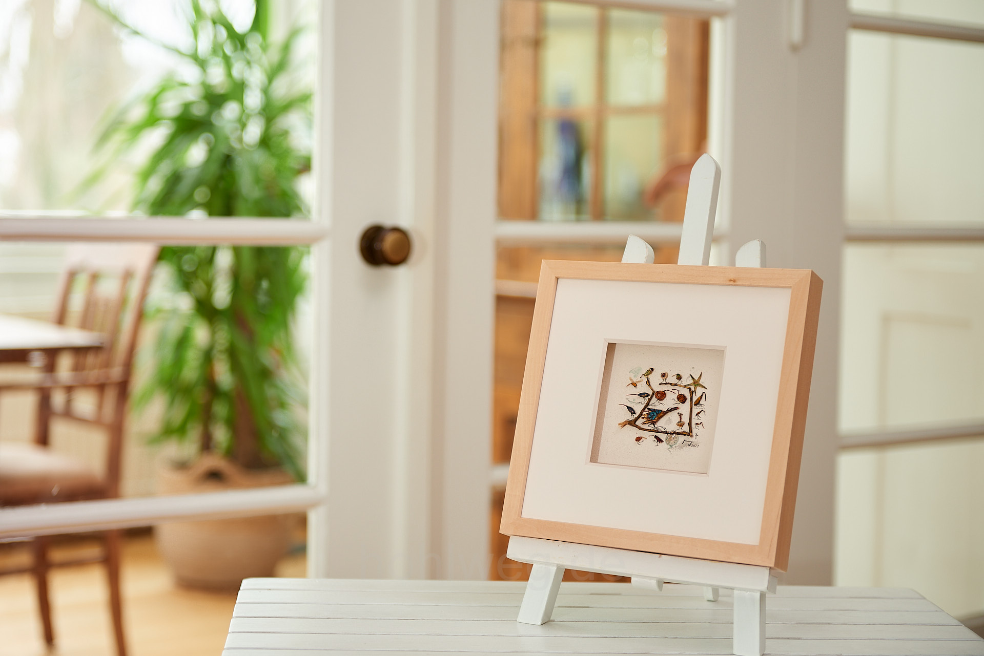 Miniaturcollage aus Fundstücken auf einem Tisch im Raum präsentiert, eingebettet in ein ruhiges Wohnambiente, das die Materialität und intime Größe des Werks sichtbar macht.