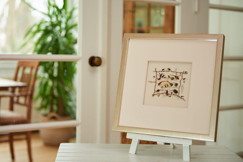 Framed collage titled “Birds Unlimited,” featuring numerous bird-like figures made from plant scraps and found objects on an easel.