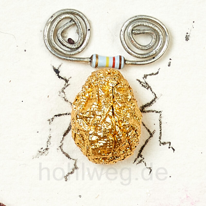 Close-up of a gold-colored beetle figurine made of chocolate wrappers, featuring an electronic resistor and spiral-shaped wires serving as antennae.
